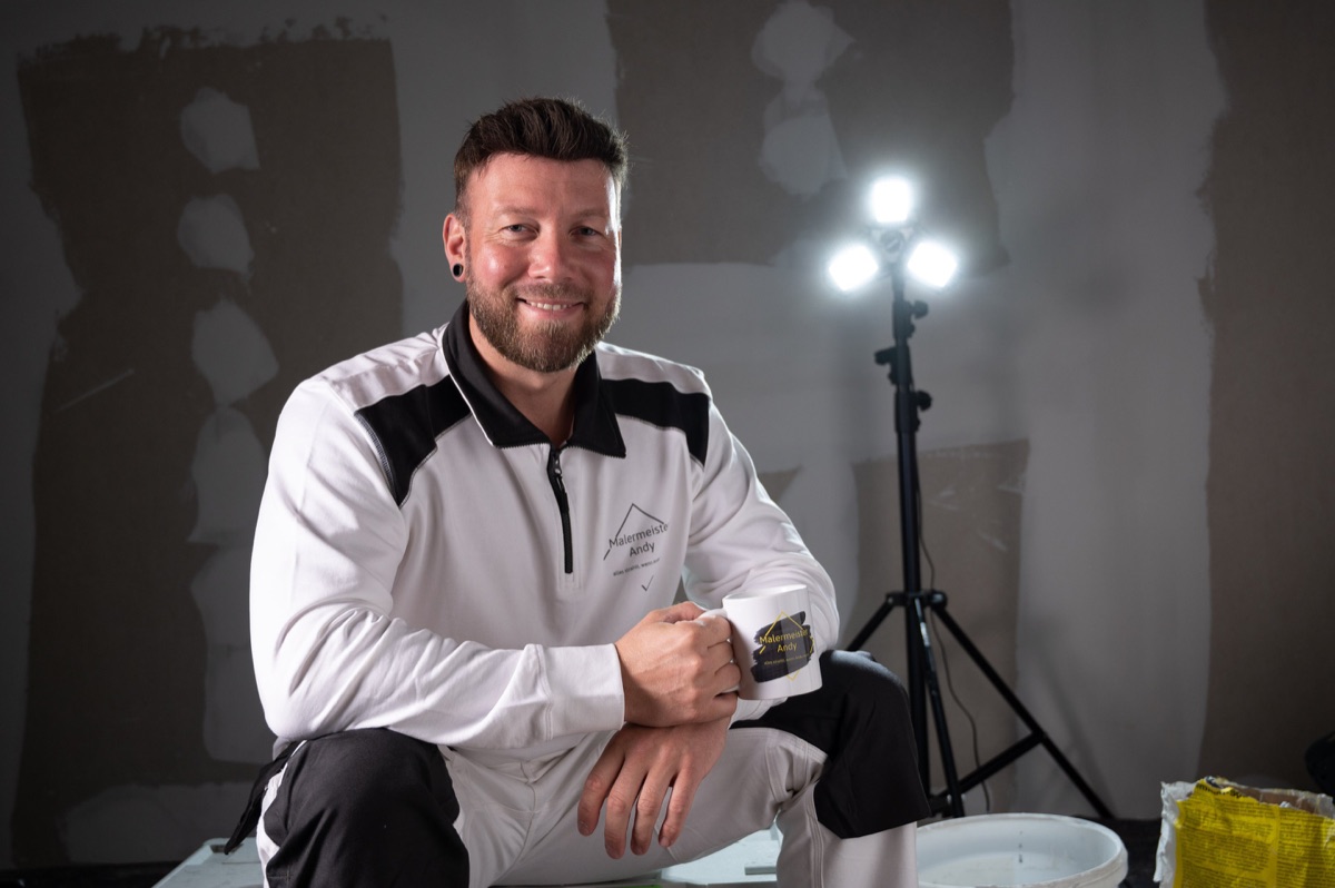 Andy Hansen, Malermeister aus Husum, sitzt lächelnd mit Kaffeebecher auf der Baustelle