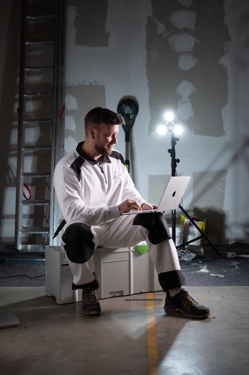 Andy Hansen sitzt mit Laptop auf der Baustelle